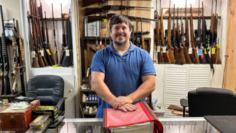 BBC James Rabun in his family's gun shop, surrounded by various types of weapons